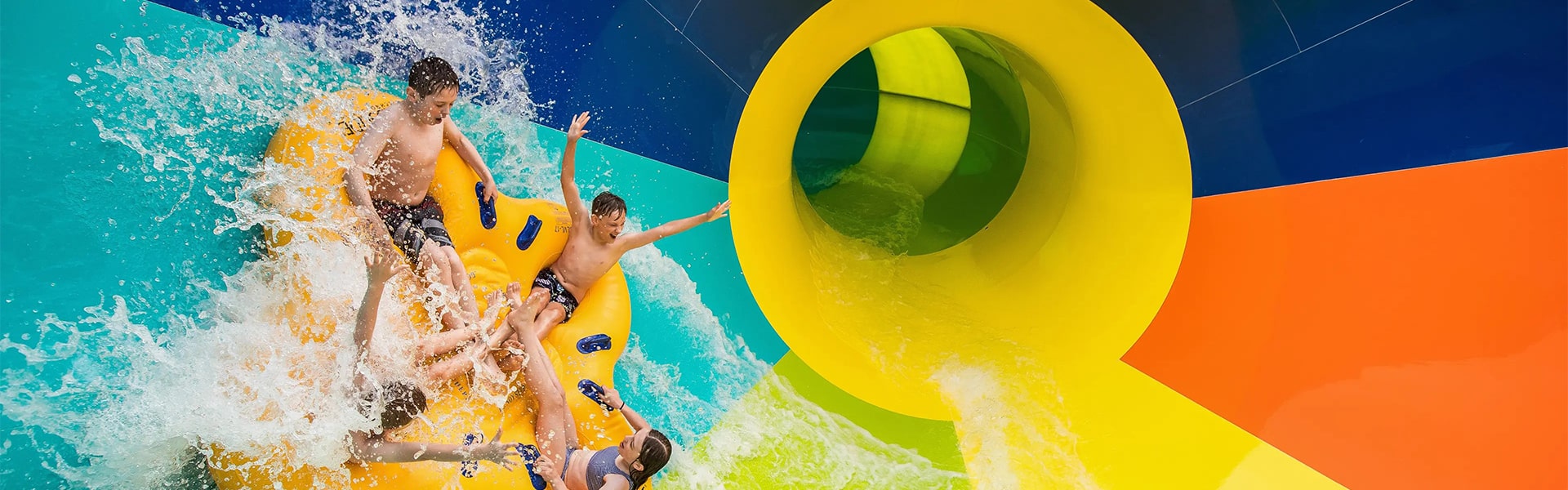 Four kids enjoying a large tornado water slide at an outdoor water park