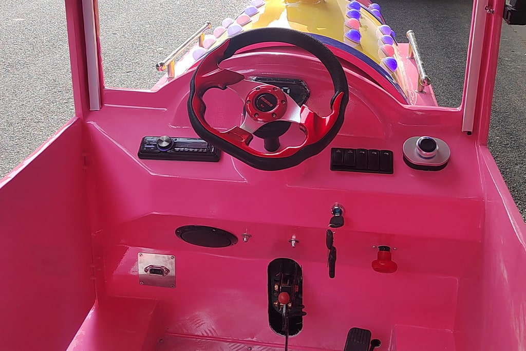 Driver’s seat close-up of a mini train ride with steering wheel and control panel.