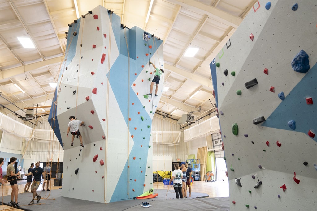 Adults climbing on a rock wall, engaging in a fun and challenging physical activity in an indoor playground.