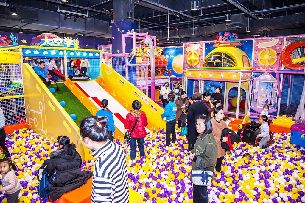 Families and kids having fun in a colorful indoor soft play zone with slides, ball pits, and foam toys.