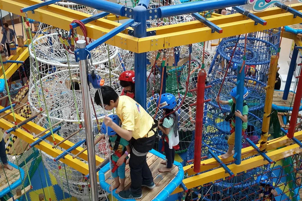Kids climbing and playing in an indoor playground inside a mall, guided by a coach.