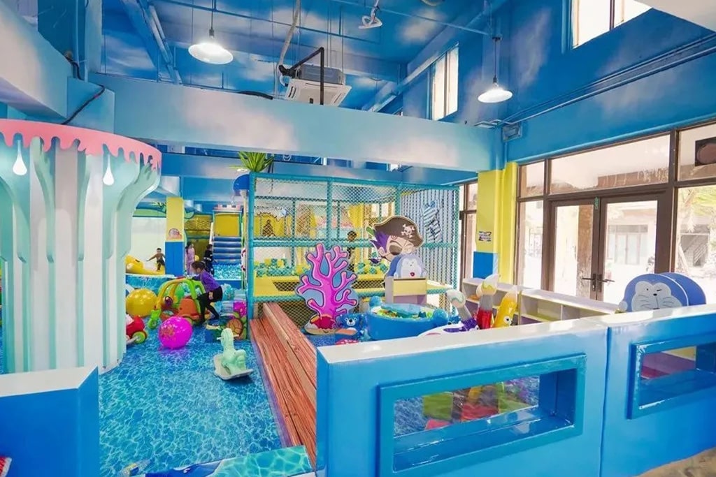 Real photo of an ocean-themed indoor playground with blue slides, soft play obstacles, and ball pits.