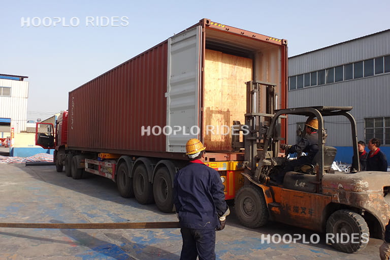 Packed wooden crates of self-control plane ride being loaded into a shipping container using forklift.
